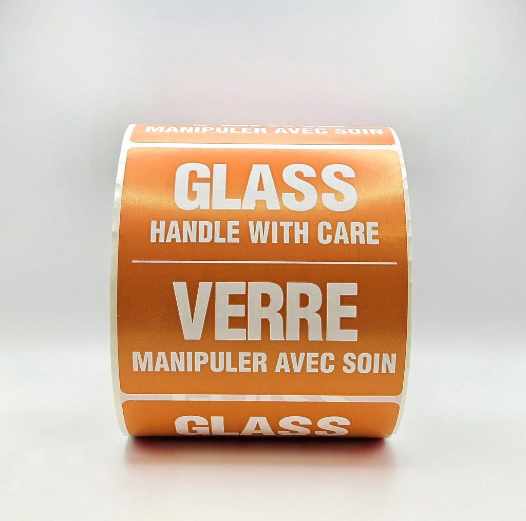 Roll of orange labels with white text warning 'Glass, handle with care' on a light gray background