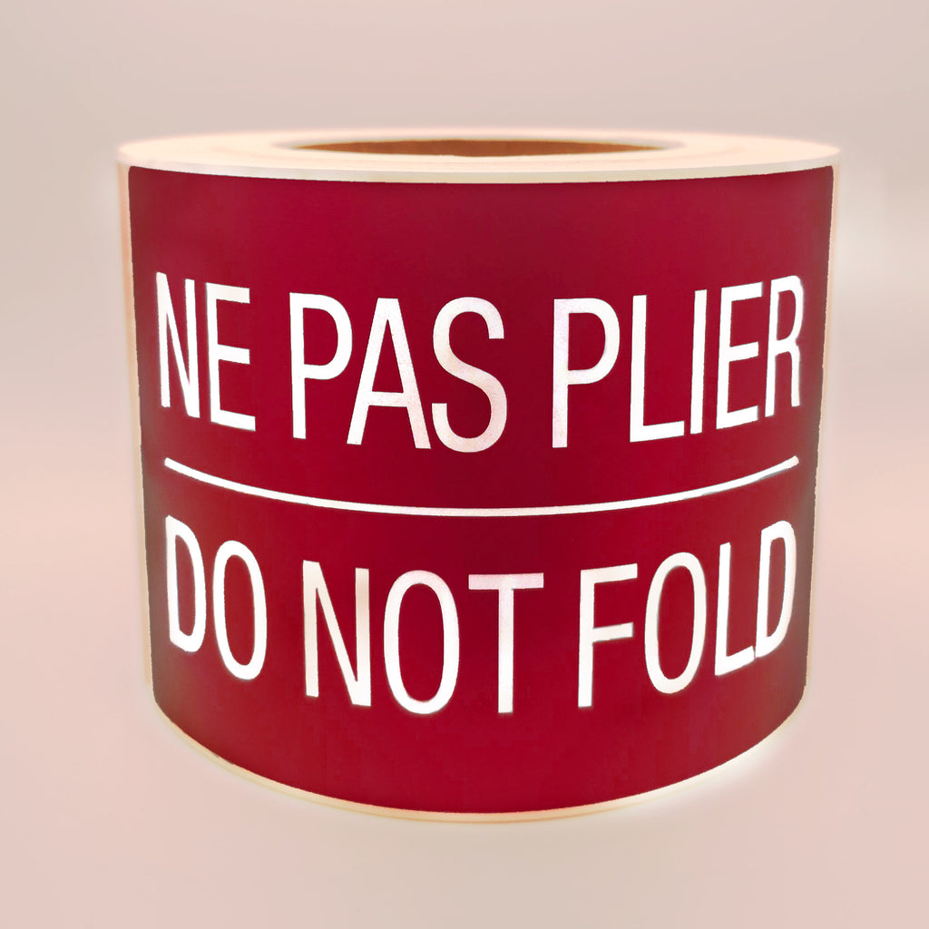 Roll of burgundy labels with white text 'NE PAS PLIER DO NOT FOLD' on a white background
