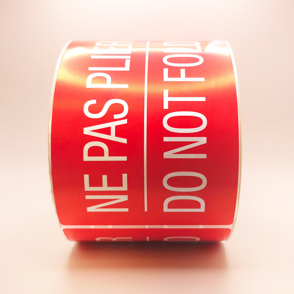 Roll of red labels with white text 'NE PAS PLIER DO NOT FOLD' on a white background front view