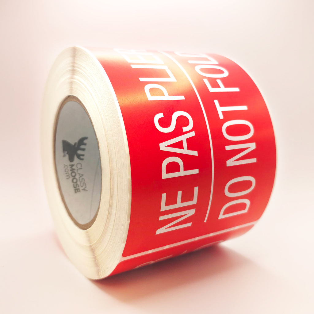 Roll of red labels with white text 'NE PAS PLIER DO NOT FOLD' on a white background side view