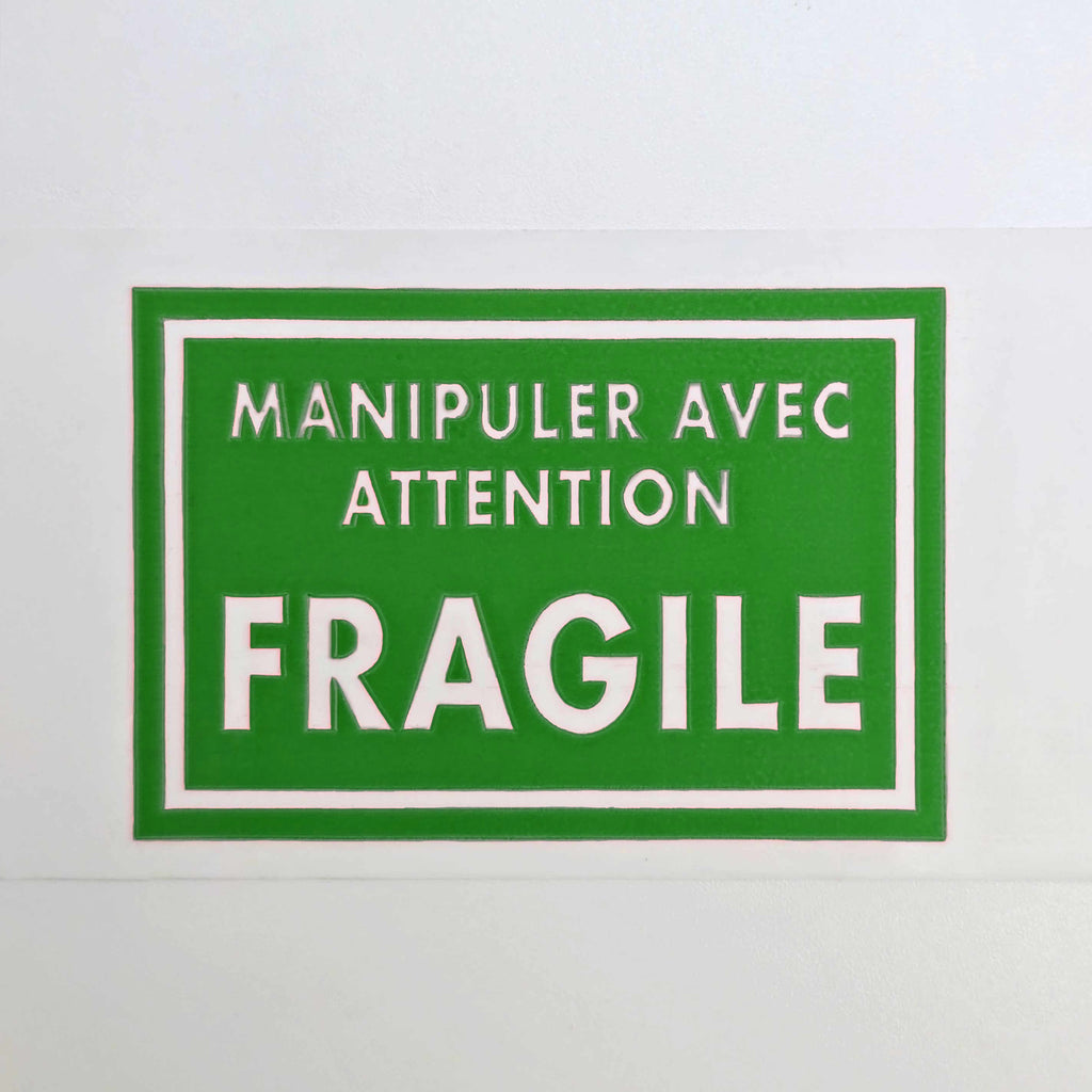 Green sign with white text 'Manipuler Avec Attention Fragile' on a white background