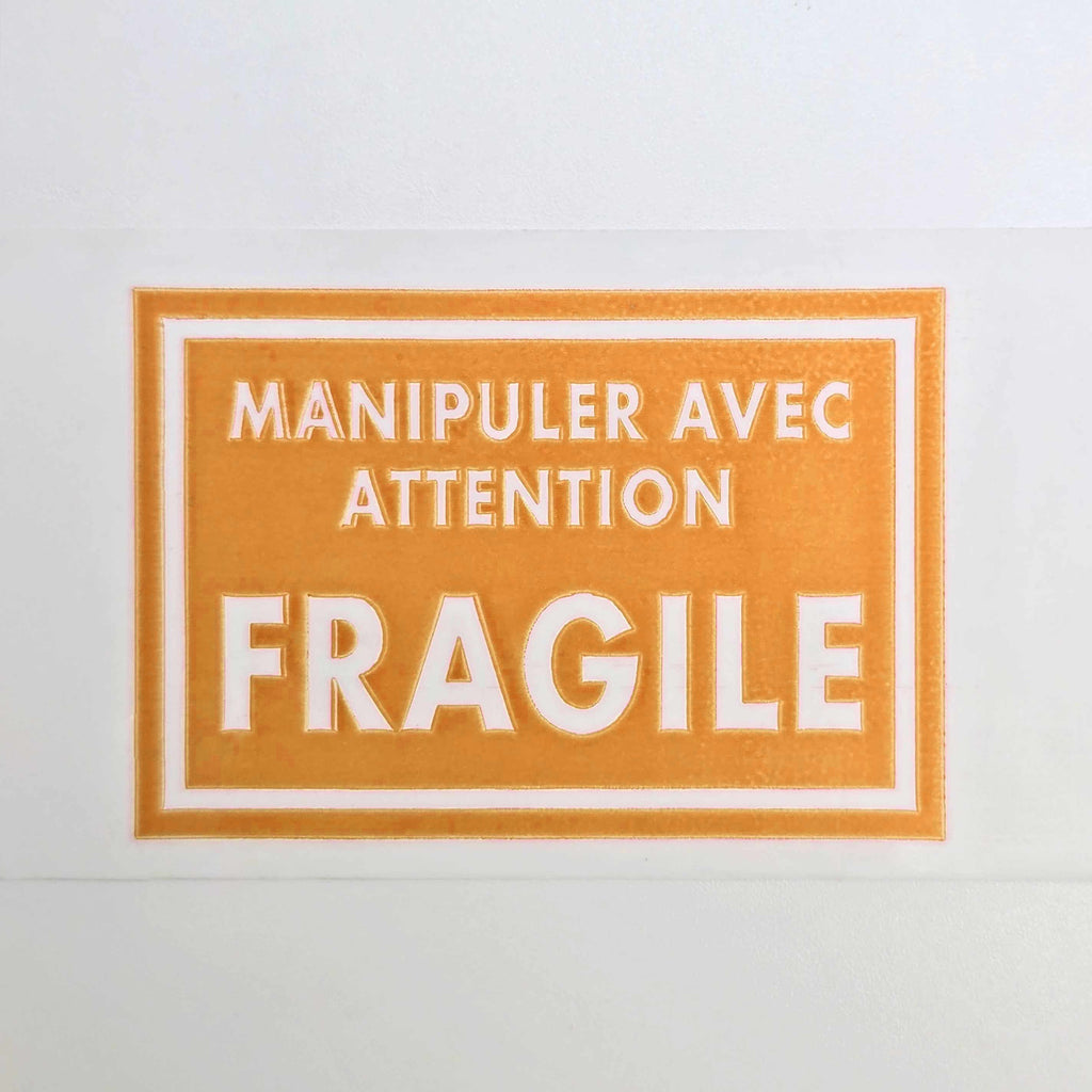 Orange label with white text 'Manipuler avec attention FRAGILE' on a white background