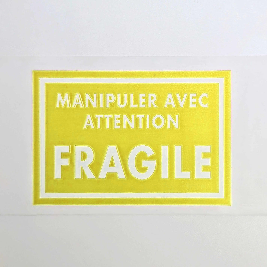 Yellow label with white text 'Manipuler avec attention FRAGILE' on a white background